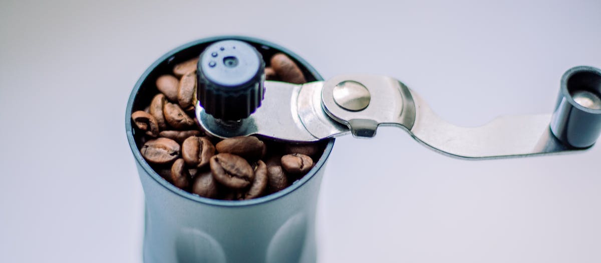 Close-up of a manual coffee grinder filled with coffee beans.