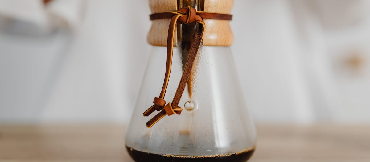 A detailed view of a Chemex coffee maker with freshly brewed drip coffee on a wooden surface.