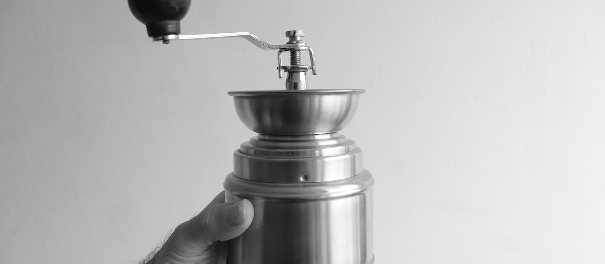 Classic black and white image of a hand holding a metal coffee grinder.